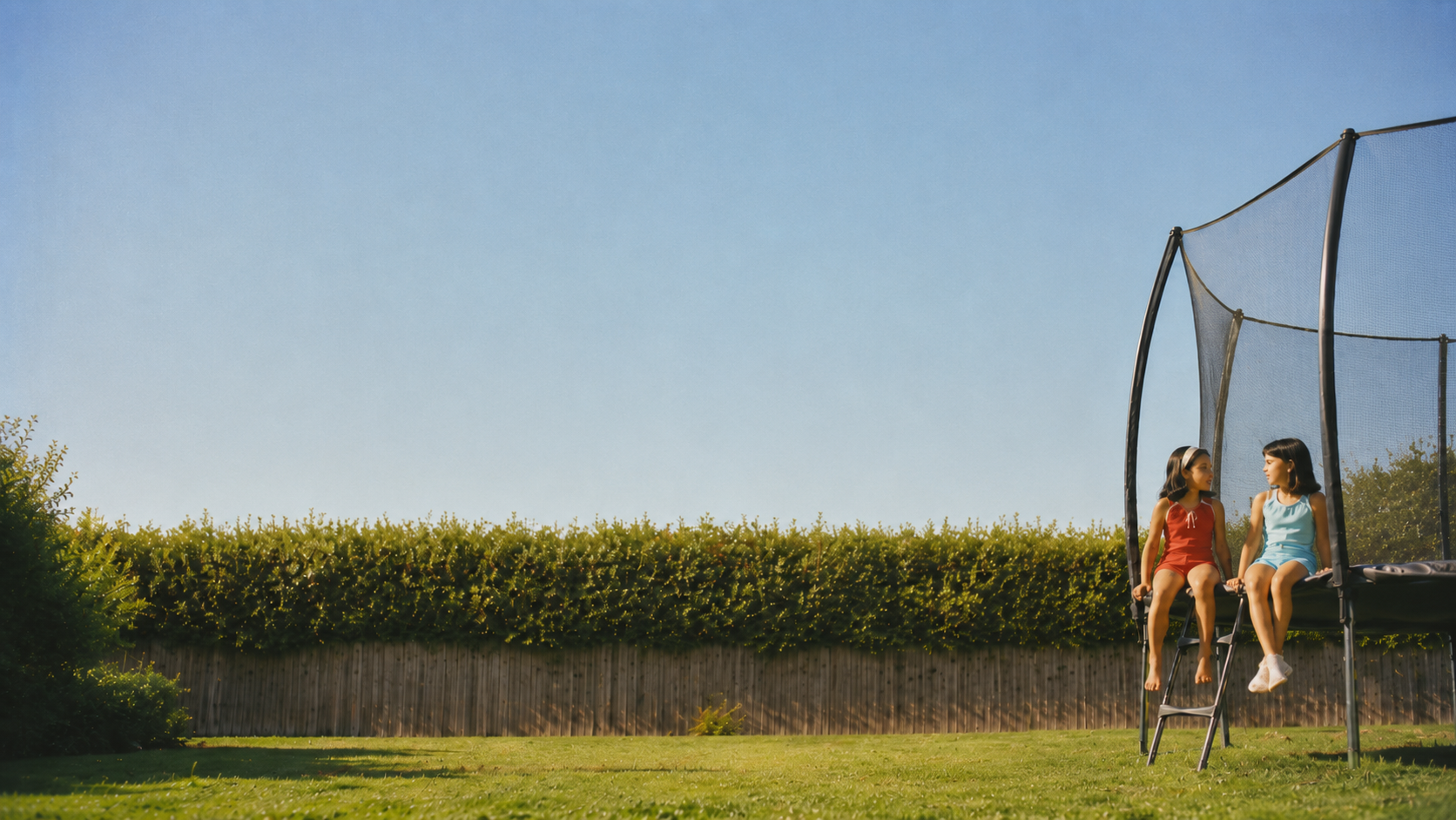 Two children sitting on a trampoline in a sunny backyard